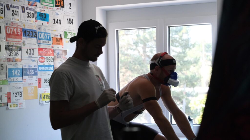 Sportwissenschaftler Massimo Köstl-Lenz überwacht bei einem Athleten am eigenen Fahrrad einen Leistungstest im Rahmen einer strukturierten Leistungsdiagnostik und kontrolliert die Daten am Laptop.