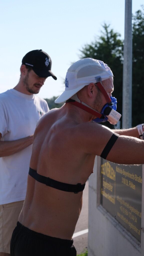 Sportwissenschaftler Massimo Köstl-Lenz begleitet einen Läufer mit VO2MASTER-Maske nach einem intensiven VO2max-Test auf der Laufstrecke und setzt mobile Leistungsdiagnostik im Ausdauersport ein.