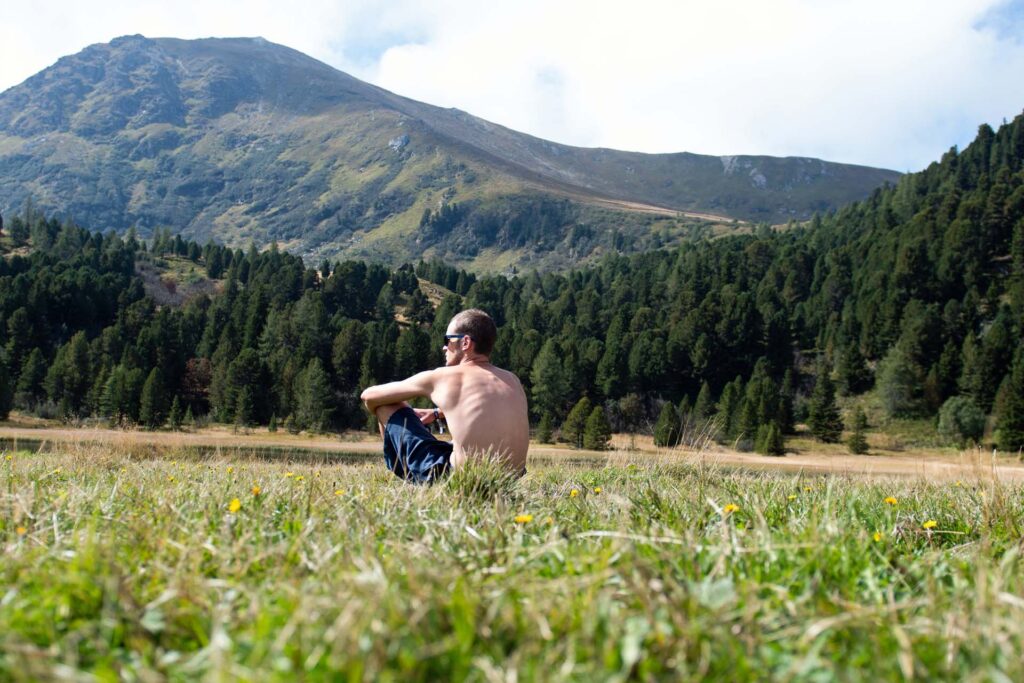 Triathlon Coach Massimo Köstl-Lenz sitzt nach dem Styrian X-treme Triathlon Steiraman im Gras vor der Bergkulisse und reflektiert den abgeschlossenen Bewerb.