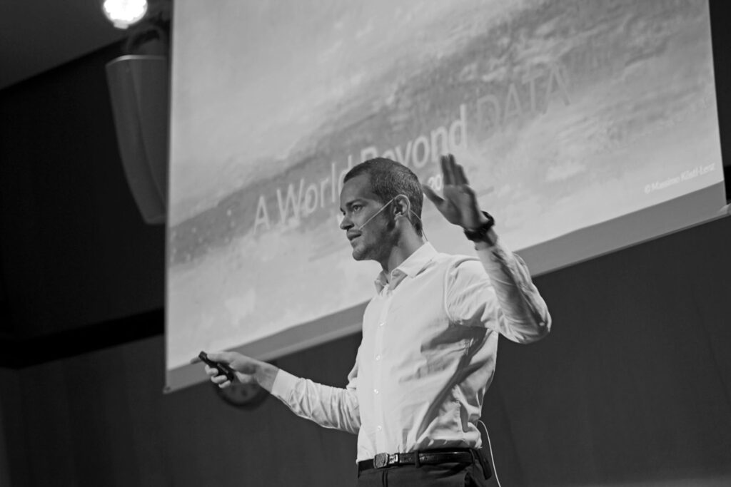 Massimo Köstl-Lenz steht als Speaker auf der Bühne, spricht mit Headset-Mikrofon vor der Präsentation „A World Beyond Data“ und teilt seine Inhalte mit dem Publikum.