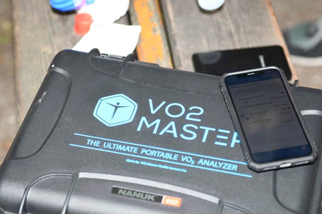 Leistungsdiagnostik im Frühjahr auf der Wiener Prater Hauptallee: Der VO₂-Master-Koffer liegt mit verbundenem Handy zur Datenübertragung auf einer Bank, vorbereitet für eine mobile Spiroergometrie Wien als Leistungstest Sport für einen Läufer im Freien.