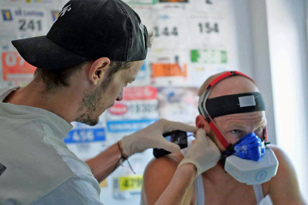 Massimo Köstl-Lenz nimmt während einer mobilen Leistungsdiagnostik zu Hause eine Laktatmessung vor; die VO₂-Master-Maske erfasst die Atemgase.