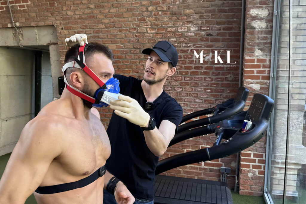 Massimo Köstl-Lenz bereitet bei einer mobilen Leistungsdiagnostik einen Athleten mit Spiroergometrie-Maske am Laufband auf die Testung vor.